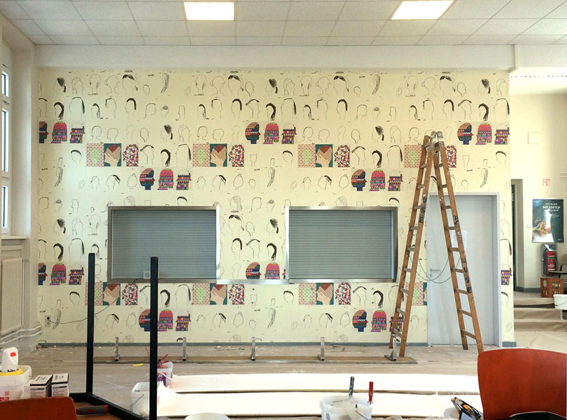 Mensa mit der Seite der Essensausgabe,  an der Wand ist die aus Kinderzeichnungen entstandene Tapete ran tapeziert von der Firma USE.